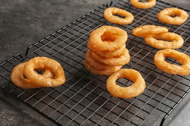 Cooling rack with tasty onion rings on table, closeup