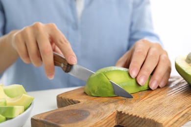 Photo of Woman cutting ripe avocado at table, closeup