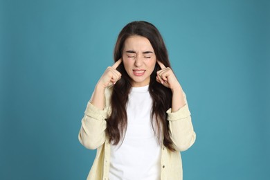 Photo of Emotional young woman covering ears with fingers on light blue background