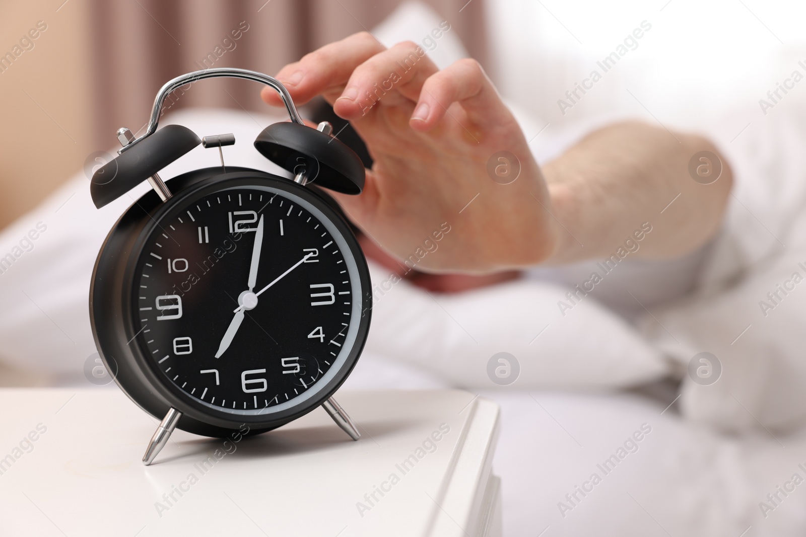 Photo of Man turning off alarm clock in bedroom, focus on hand
