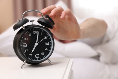 Photo of Man turning off alarm clock in bedroom, focus on hand