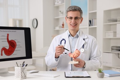 Photo of Gastroenterologist showing human stomach model at table in clinic