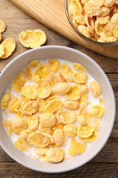 Photo of Tasty cornflakes with milk in bowl on wooden table, flat lay
