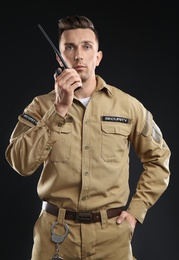 Male security guard using portable radio transmitter on dark background