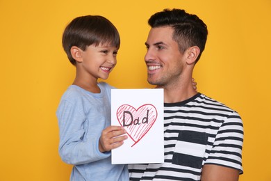 Photo of Little boy greeting his dad with Father's Day on yellow background