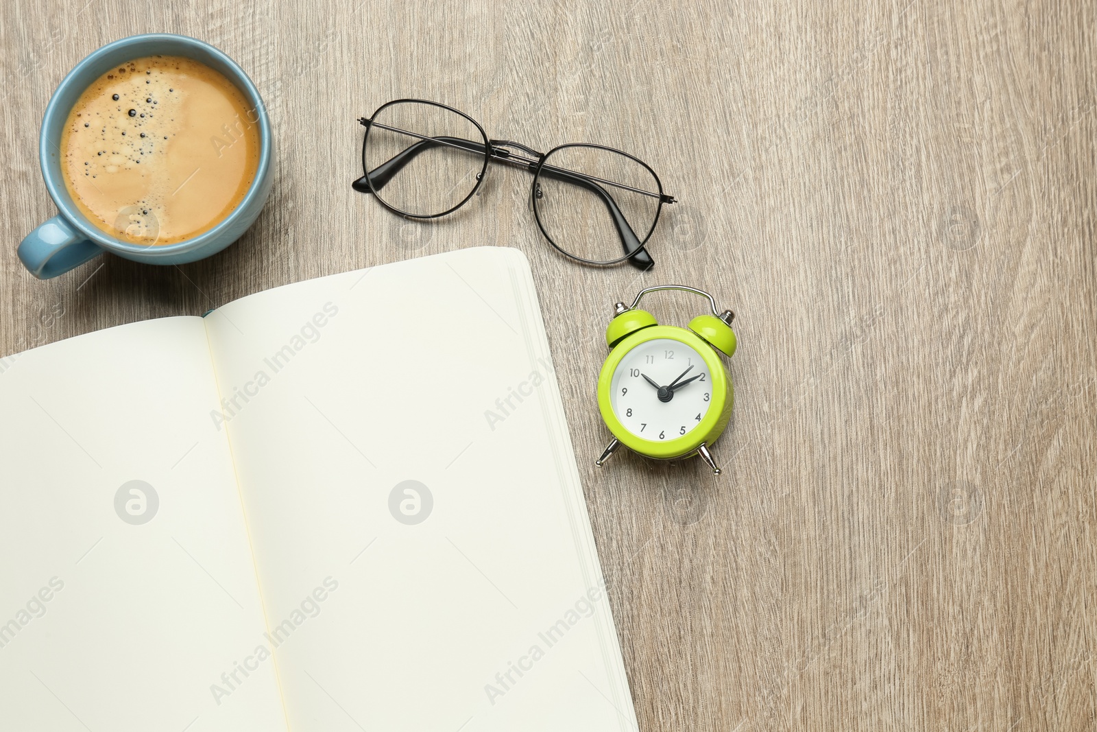 Photo of Open notebook, glasses, alarm clock and cup of coffee on wooden table, flat lay. Space for text