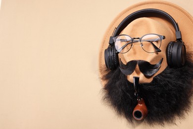 Photo of Man's face made of artificial mustache, beard, glasses and hat on beige background, top view. Space for text