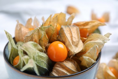 Photo of Ripe physalis fruits with dry husk in bowl, closeup