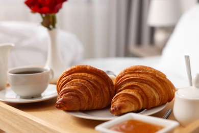 Photo of Tasty breakfast served in bed. Fresh croissants, coffee and honey on wooden tray, closeup
