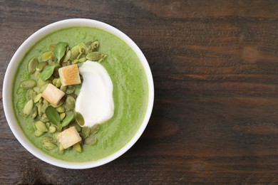 Photo of Delicious broccoli cream soup with croutons, sour cream and pumpkin seeds on wooden table, top view. Space for text