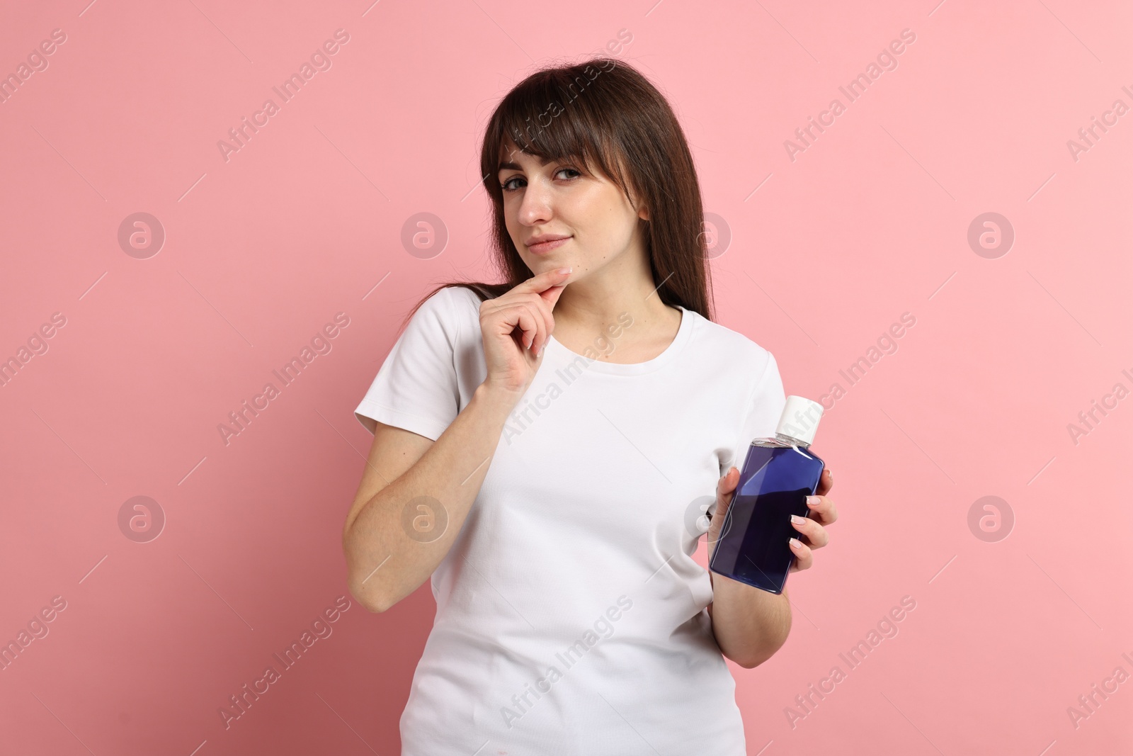 Photo of Thoughtful young woman with mouthwash on pink background