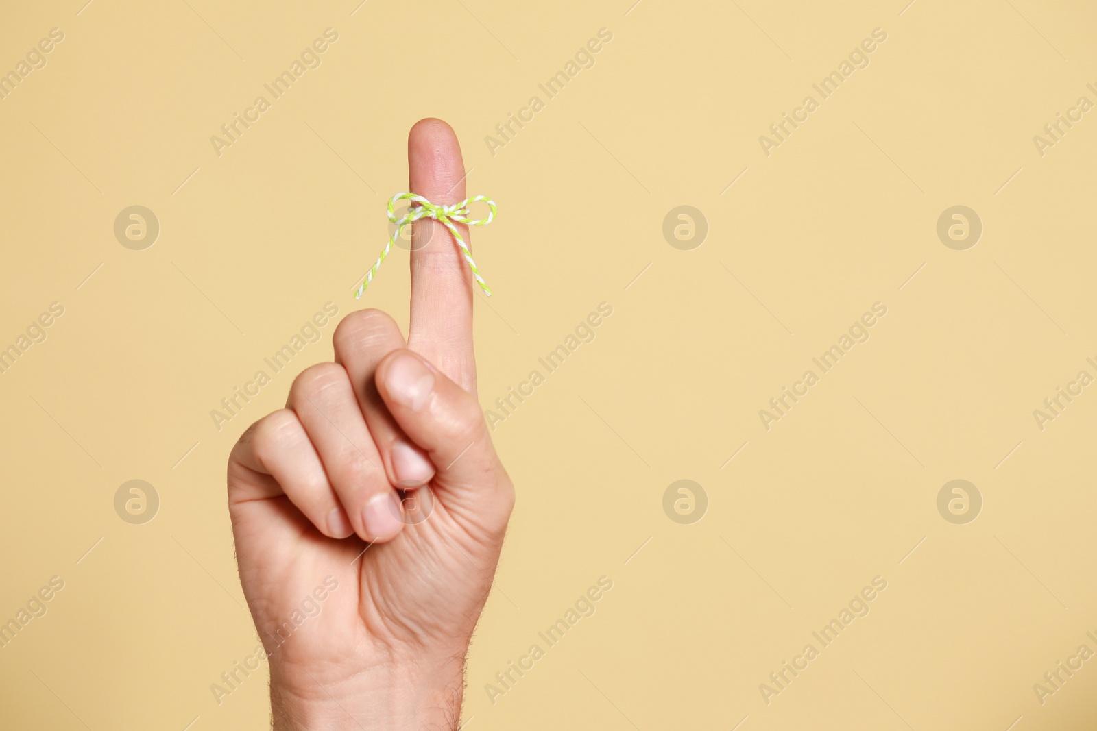 Photo of Man showing index finger with tied bow as reminder on beige background, closeup. Space for text