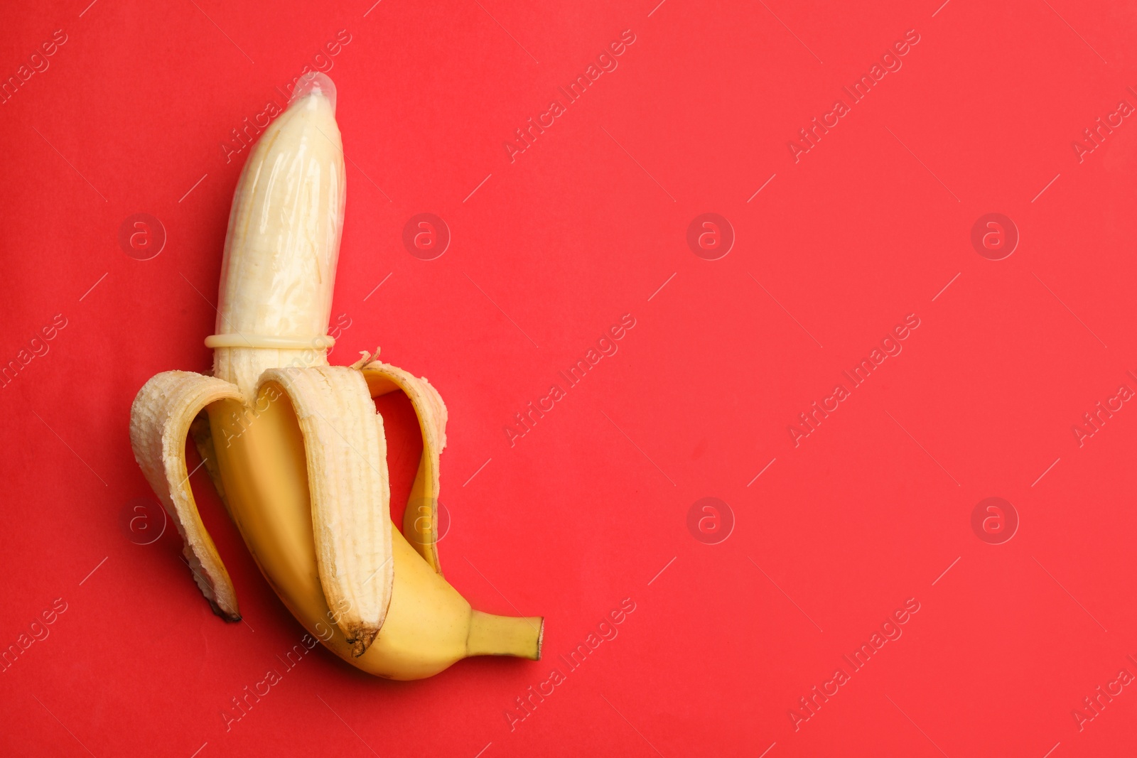 Photo of Banana with condom and space for text on red background, top view. Safe sex