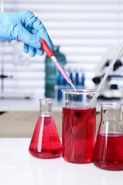 Photo of Laboratory analysis. Woman dripping red liquid into beaker on white table, closeup