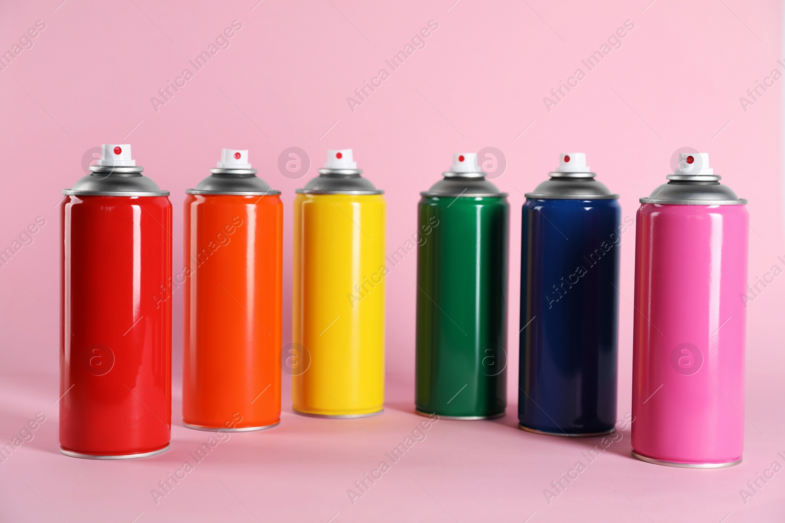 Photo of Colorful cans of spray paints on pink background