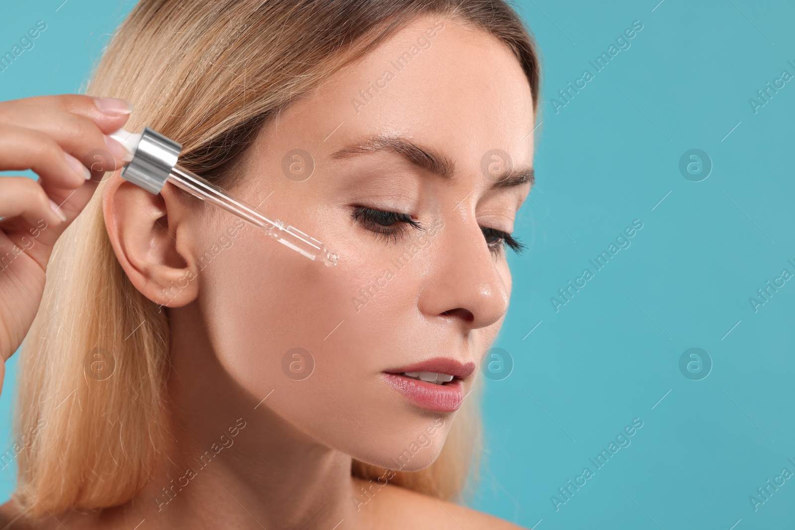 Photo of Beautiful woman applying cosmetic serum onto her face on light blue background, closeup. Space for text