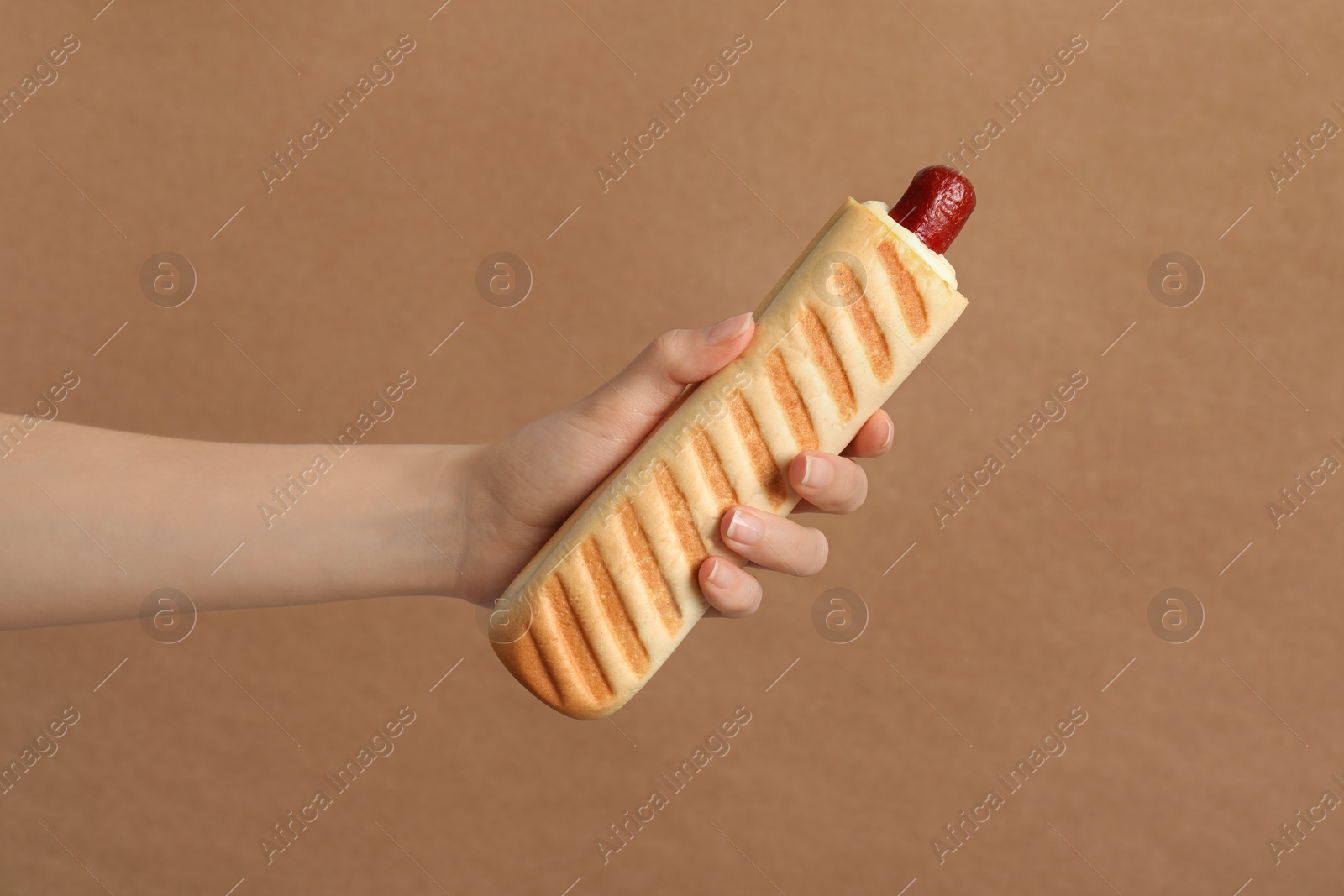 Photo of Woman holding delicious french hot dog on brown background, closeup