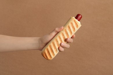 Photo of Woman holding delicious french hot dog on brown background, closeup