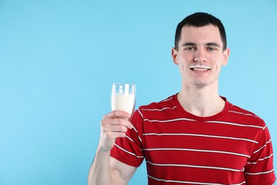 Photo of Happy man with milk mustache holding glass of tasty dairy drink on light blue background, space for text