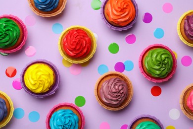 Photo of Many delicious colorful cupcakes and confetti on violet background, flat lay