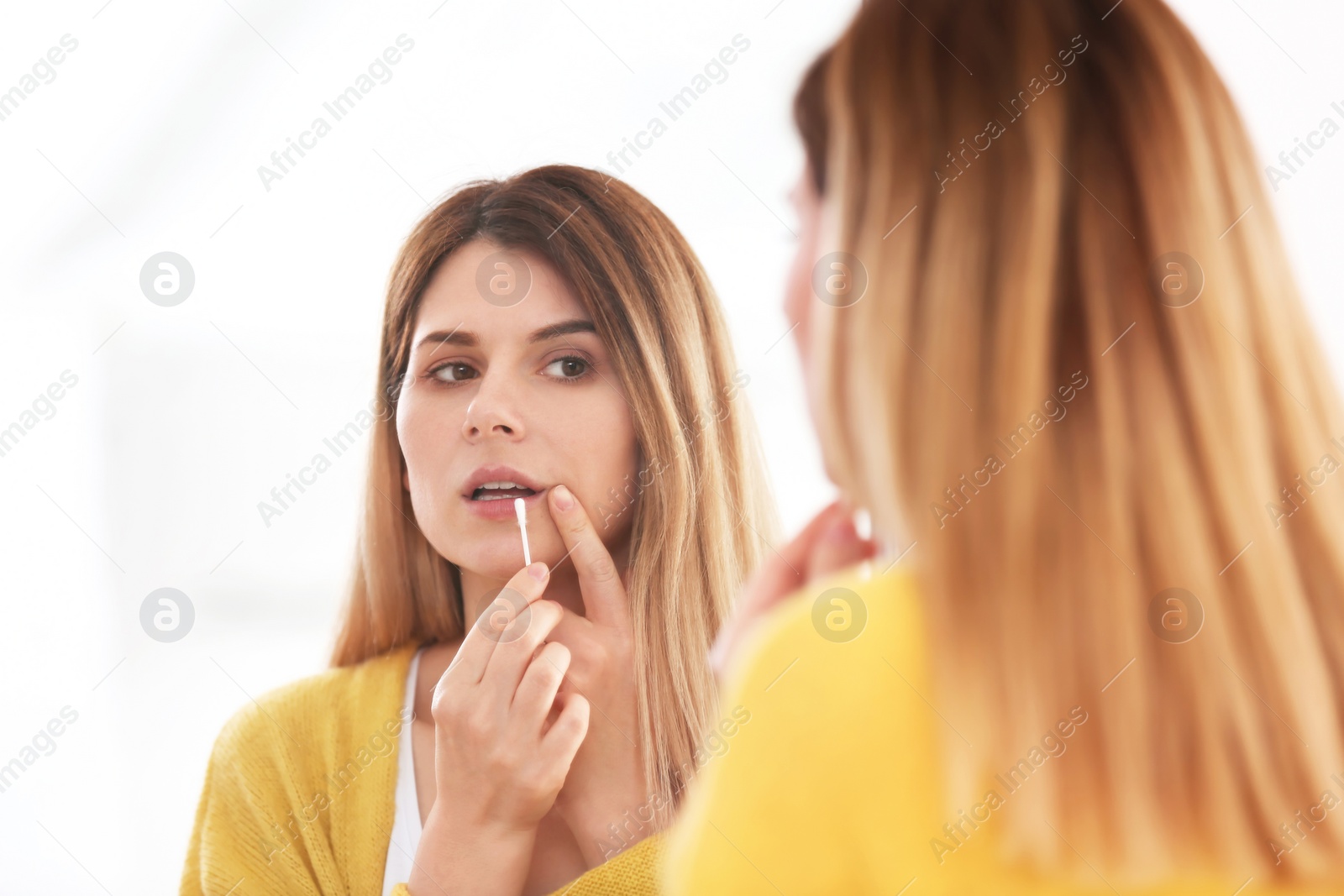 Photo of Woman applying cold sore cream on lips in front of mirror
