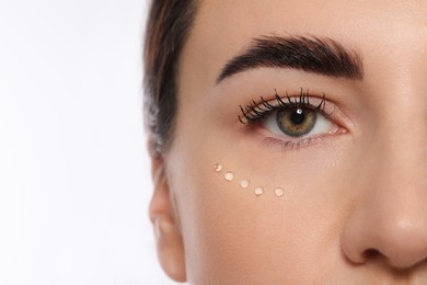 Woman with cosmetic product around eye on white background, closeup. Skin care