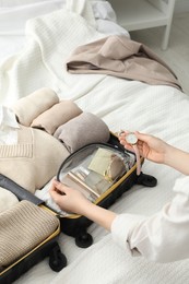 Photo of Woman holding wristwatch near open suitcase on bed. closeup