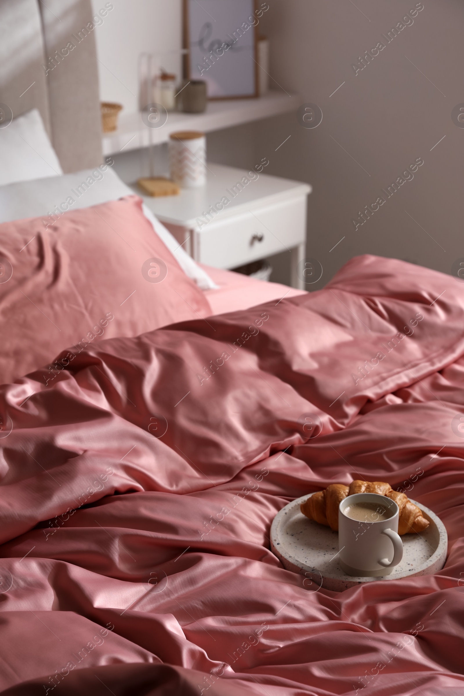 Photo of Breakfast tray on bed with beautiful pink silk linens indoors