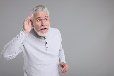 Portrait of surprised senior man on grey background, space for text