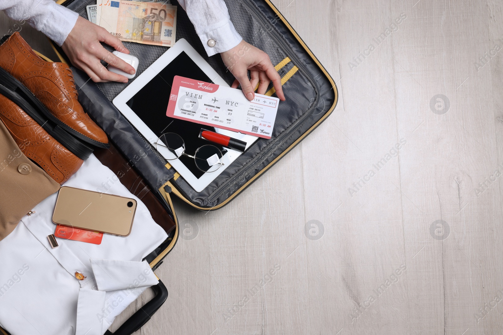 Photo of Woman packing suitcase for business trip on wooden floor, top view