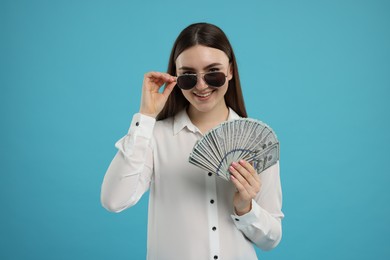 Happy woman with dollar banknotes on light blue background