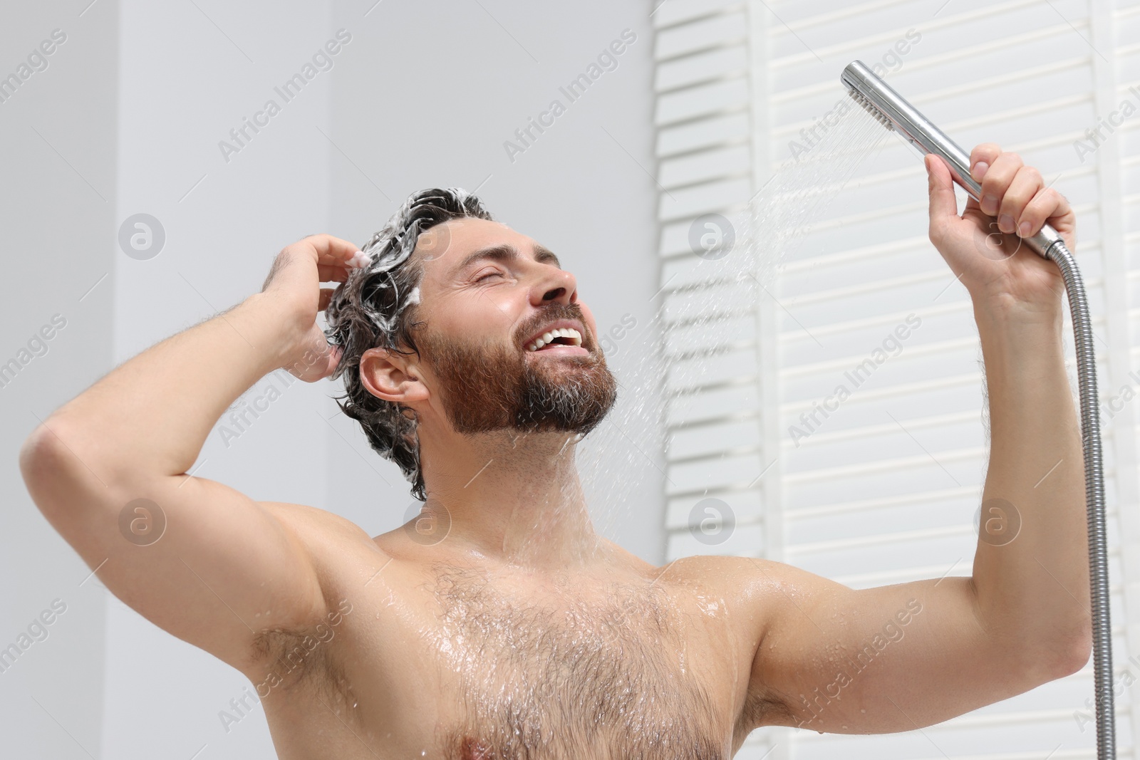 Photo of Happy man washing his hair with shampoo in shower