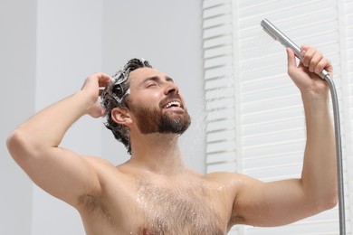 Photo of Happy man washing his hair with shampoo in shower