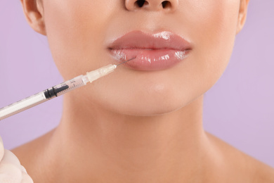 Young woman getting lips injection on lilac background, closeup