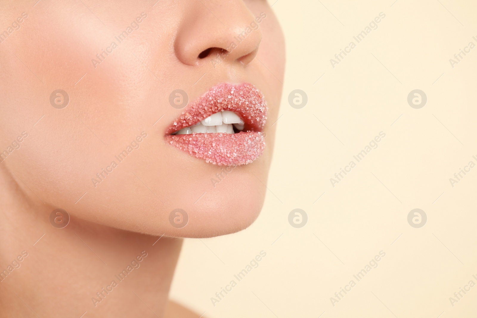 Photo of Young woman with sugar scrub on lips against beige background, closeup