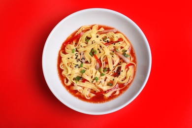 Plate of asian noodles with broth and vegetables on color background, top view