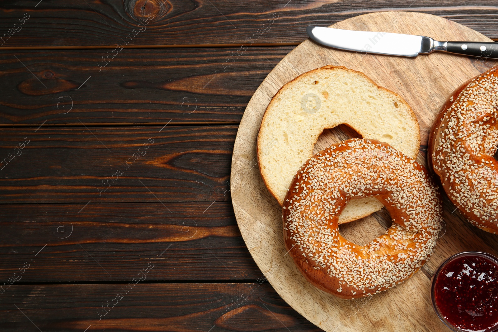 Photo of Delicious fresh bagels with sesame seeds and jam on wooden table, top view. Space for text