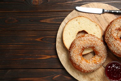 Photo of Delicious fresh bagels with sesame seeds and jam on wooden table, top view. Space for text