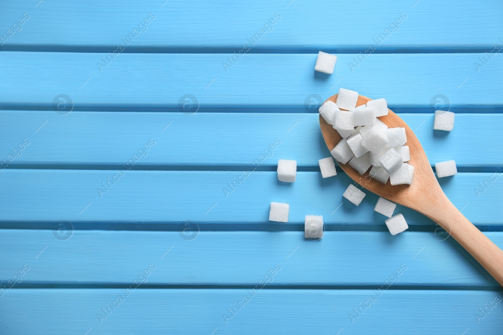 Photo of Spoon with refined sugar cubes on color wooden background, top view