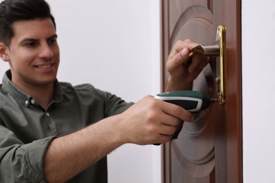 Handyman with screw gun repairing door lock indoors, focus on hand