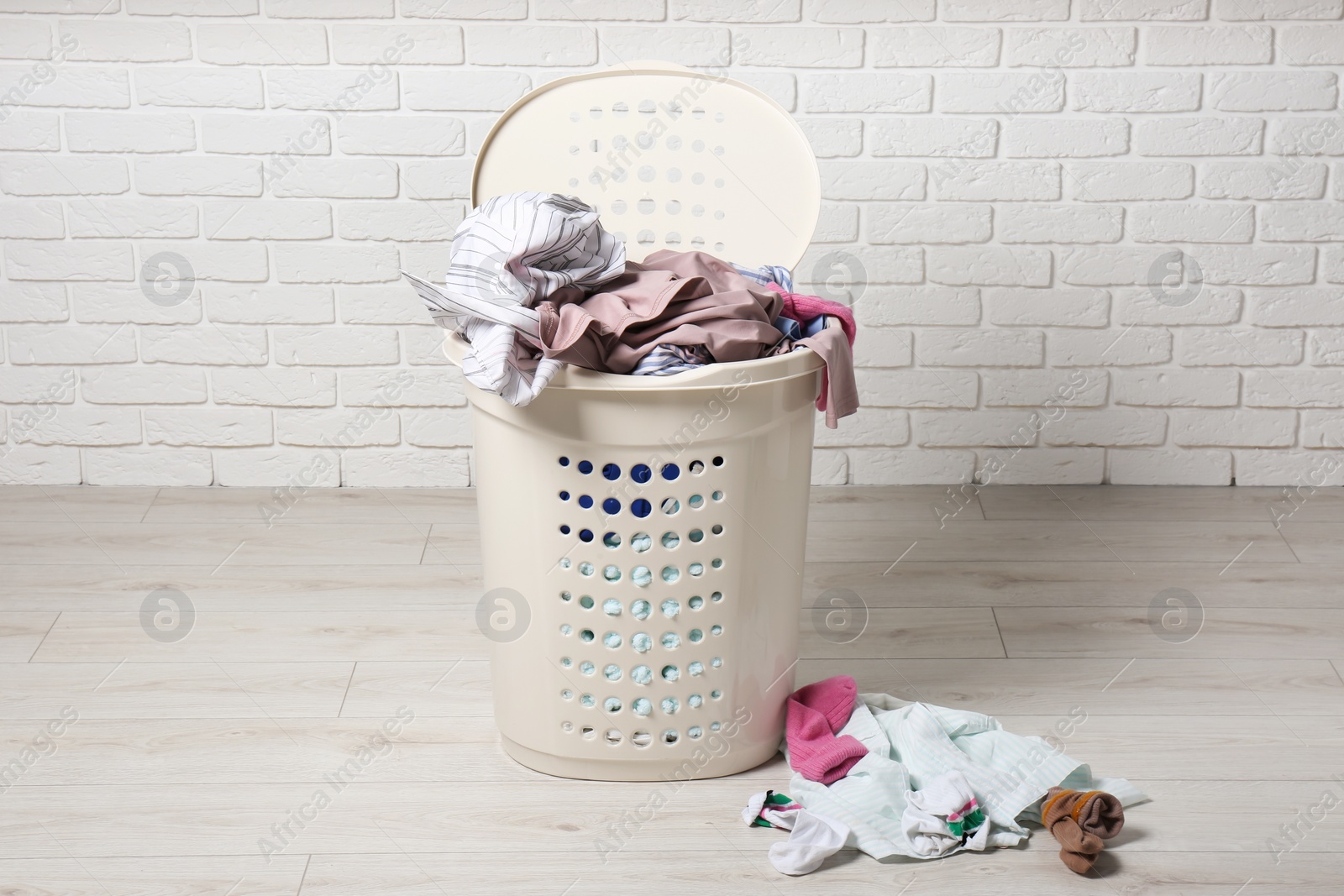 Photo of Laundry basket with clothes near white brick wall