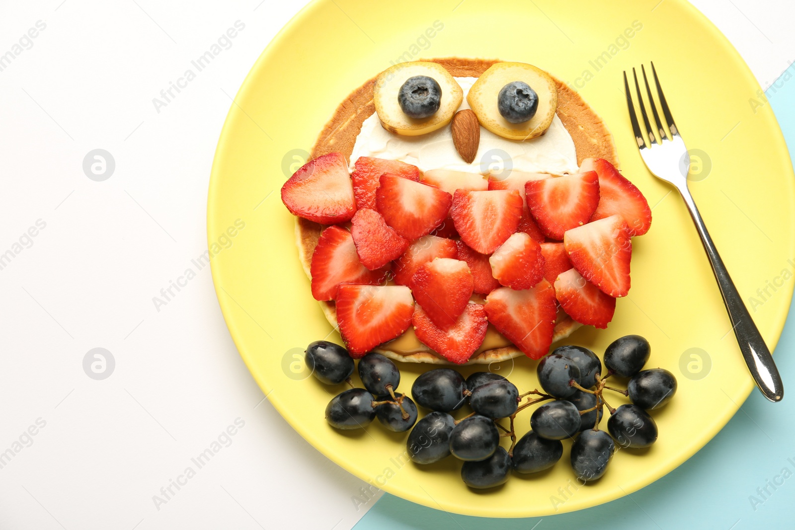 Photo of Creative serving for kids. Plate with cute owl made of pancakes, berries, cream, banana and almond on color background, top view. Space for text