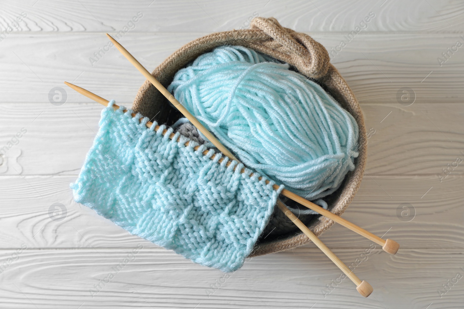 Photo of Soft turquoise yarn, knitting and needles on white wooden table, top view