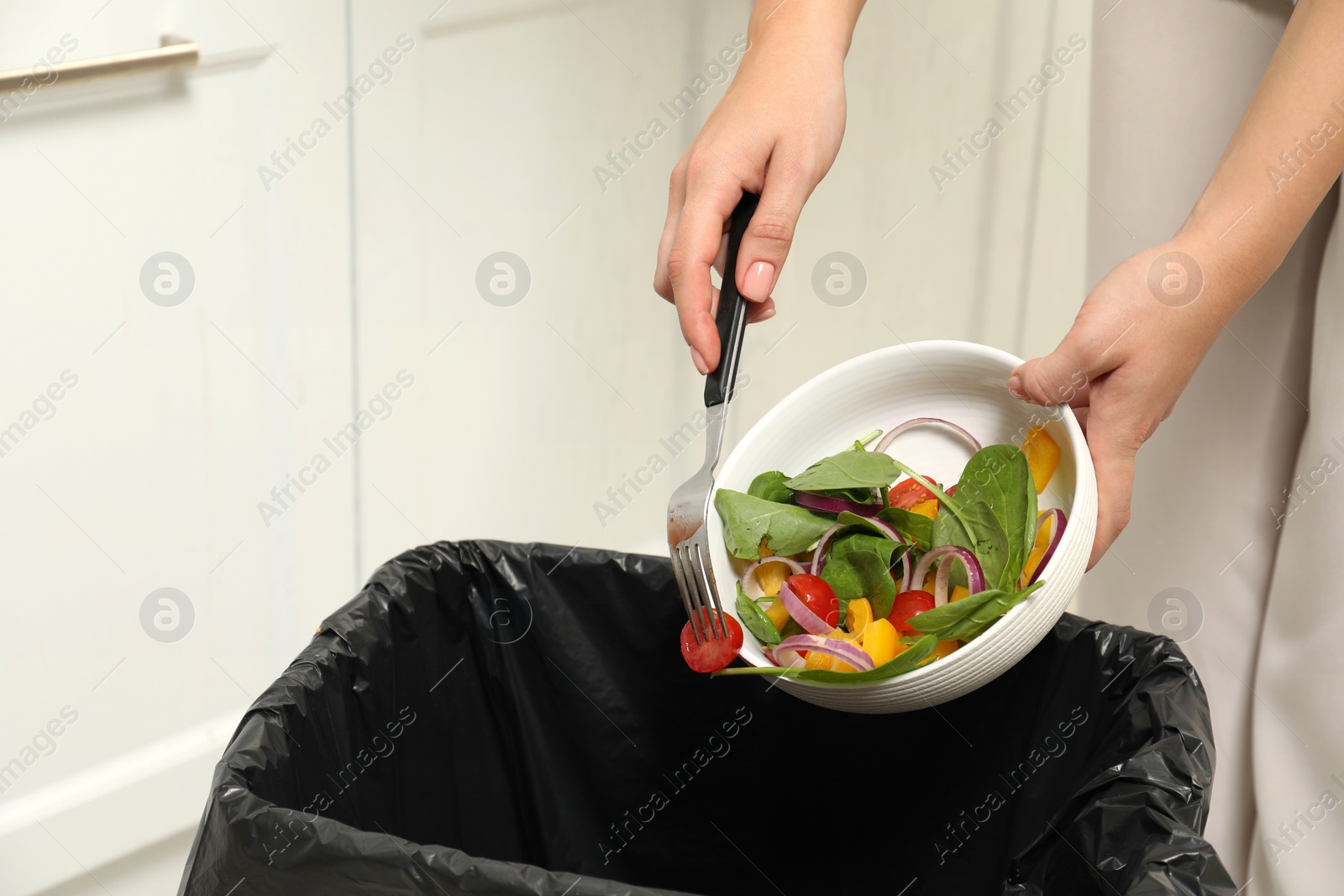 Photo of Woman throwing vegetable salad into bin indoors, closeup. Space for text