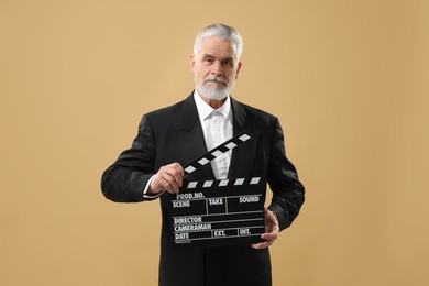 Photo of Senior actor holding clapperboard on beige background. Film industry