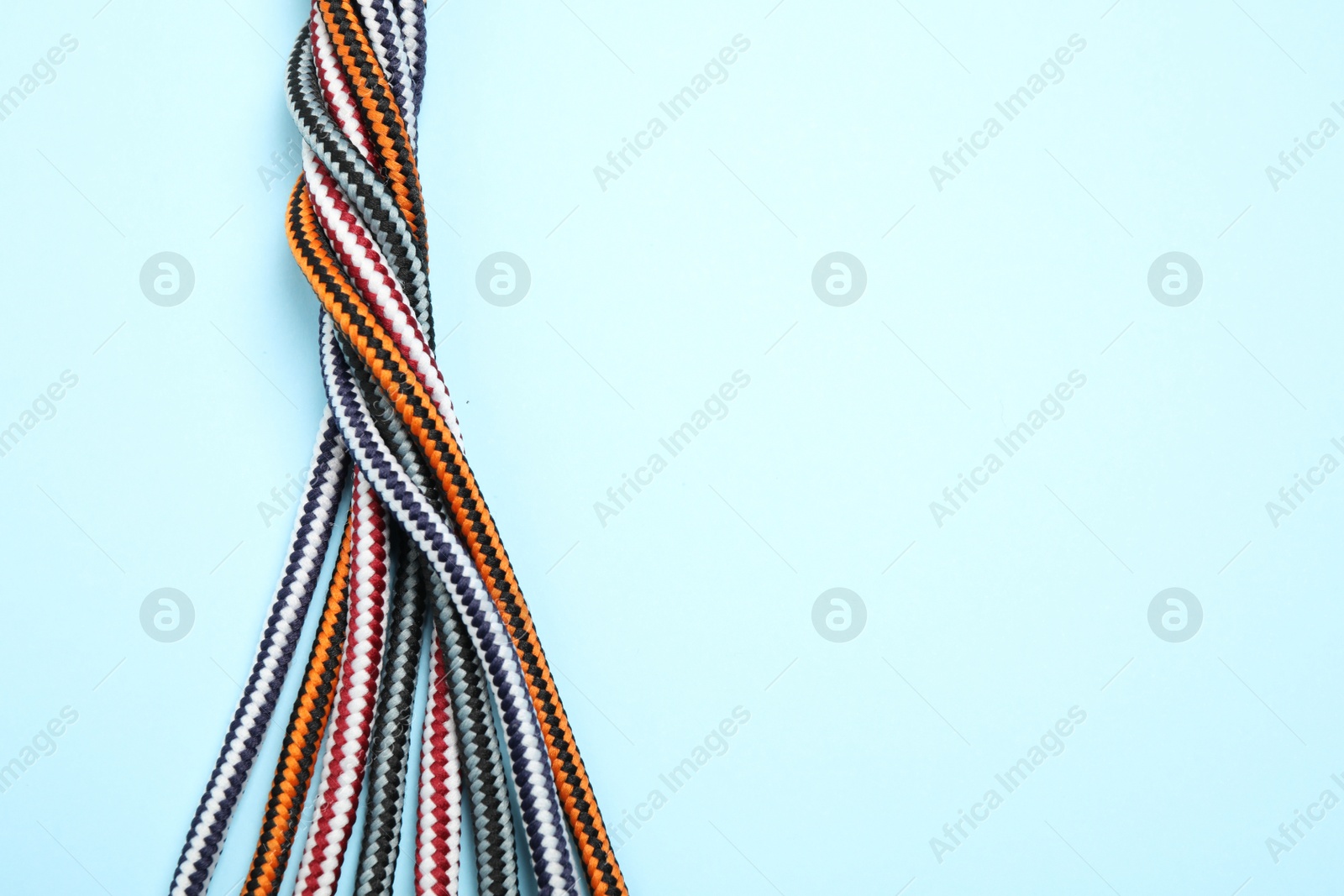 Photo of Top view of twisted colorful ropes on light blue background, space for text. Unity concept