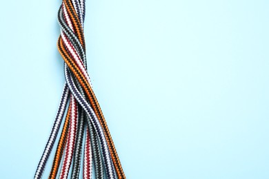 Photo of Top view of twisted colorful ropes on light blue background, space for text. Unity concept