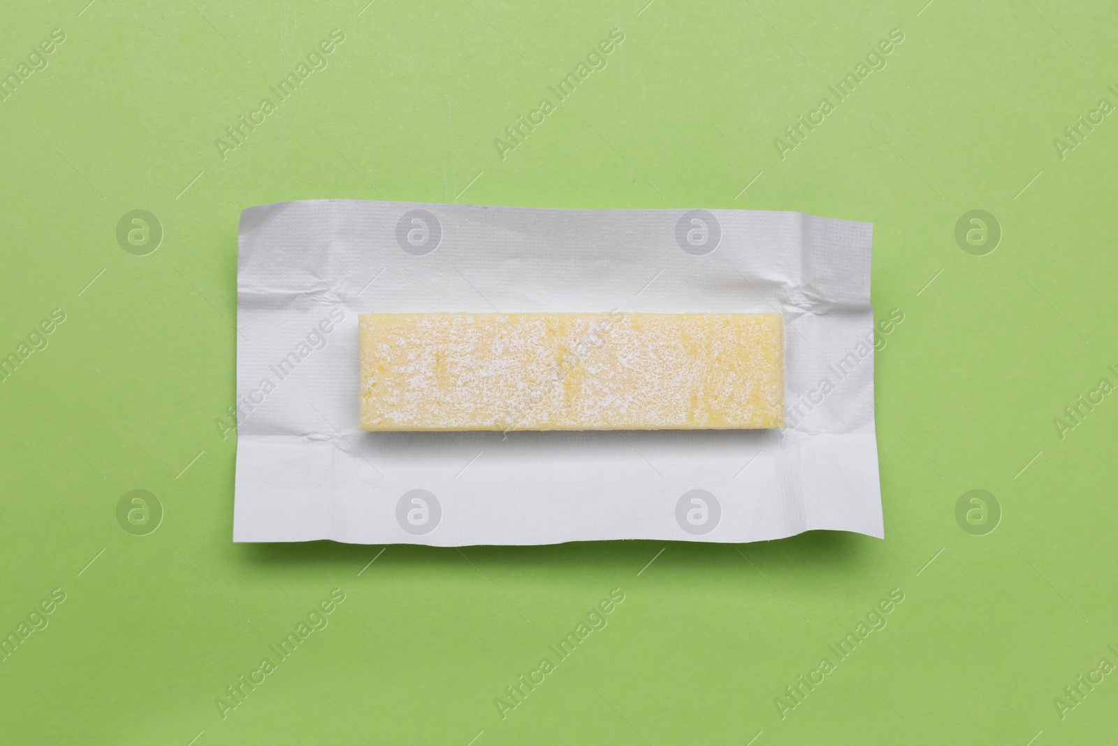 Photo of Unwrapped stick of chewing gum on light green background, top view