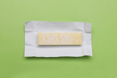 Photo of Unwrapped stick of chewing gum on light green background, top view
