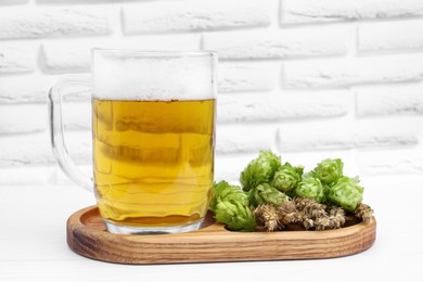 Photo of Mug with beer, fresh hops and ears of wheat on white wooden table